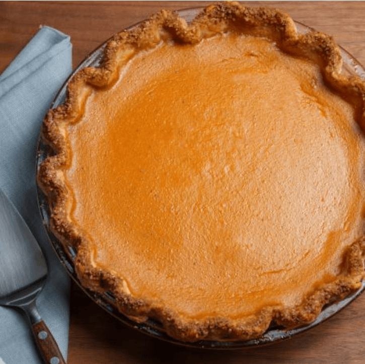 A cooked pumpkin pie sitting on a wood table with a blue napkin