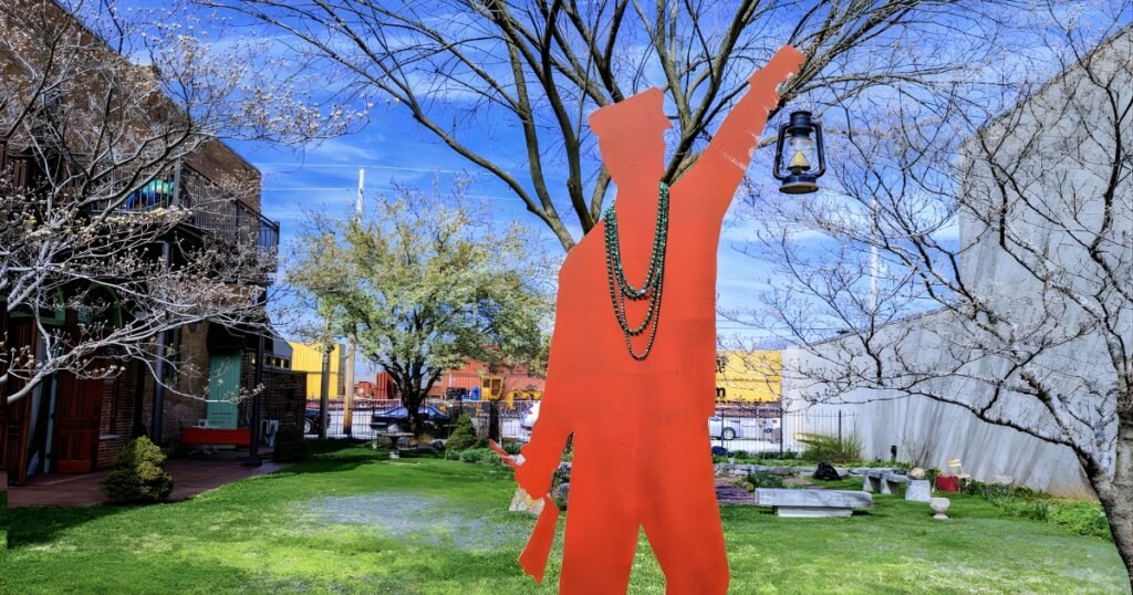 Red human sculpture holding a lantern on a spring lawn along Historic Commercial Street, Springfield, Missouri.