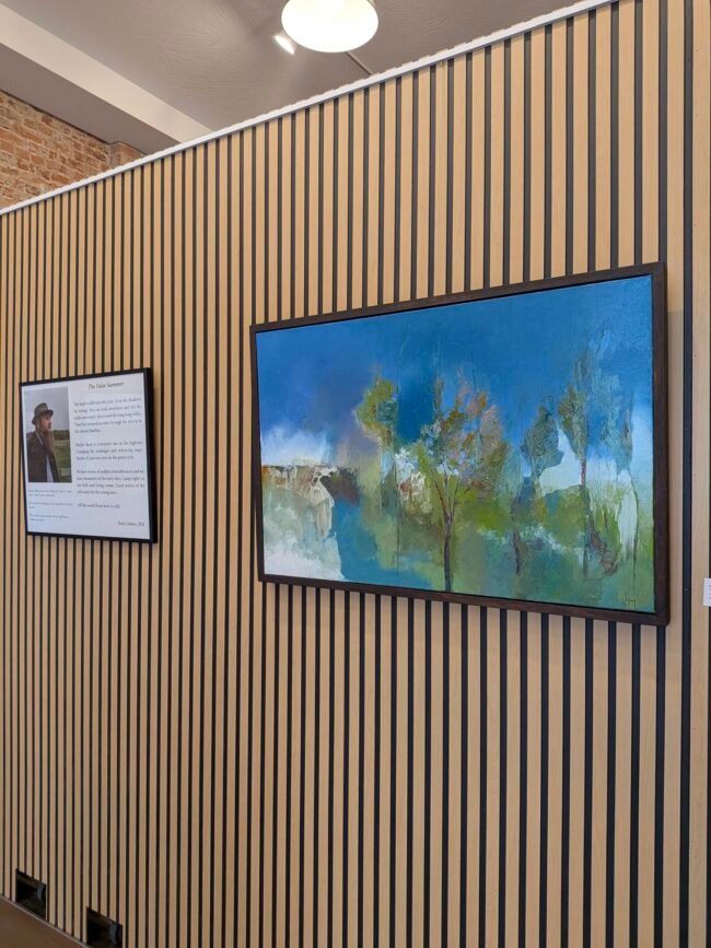 A Rusty Lindsey landscape beside its artist statement on a slat wall at C-ART Gallery on C-Street.