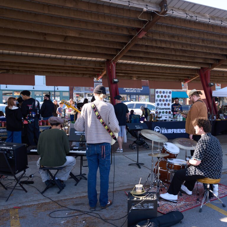 A youth band performs at the C-Street City Market as shoppers browse the vendor booths.