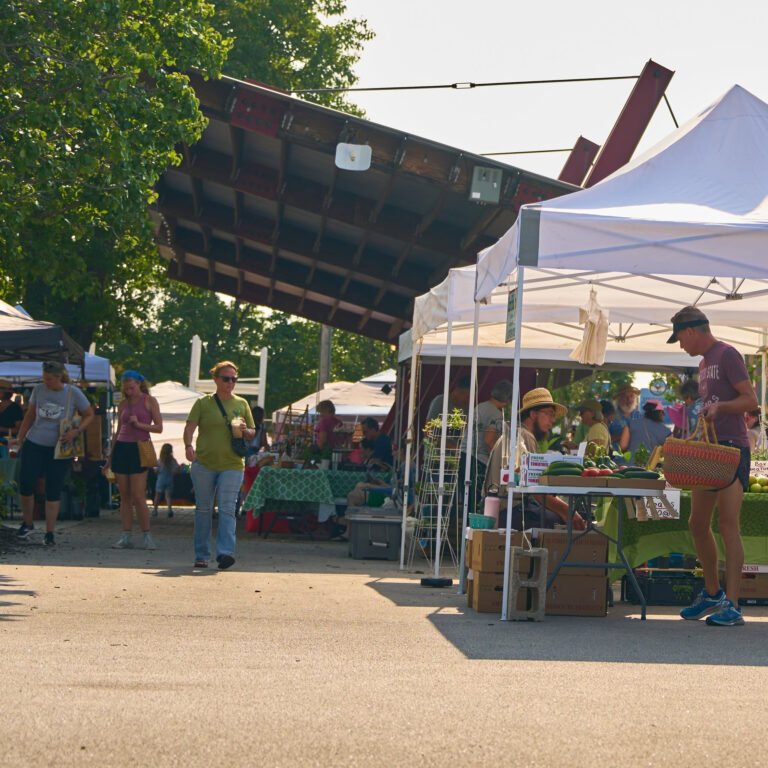 Shoppers stroll the C-Street City Market past produce tents under the historic beam pavilion.