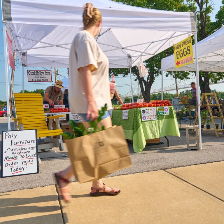 A shopper carries a paper bag past the Ozark Hollow Farm produce stand at the C-Street City Market.