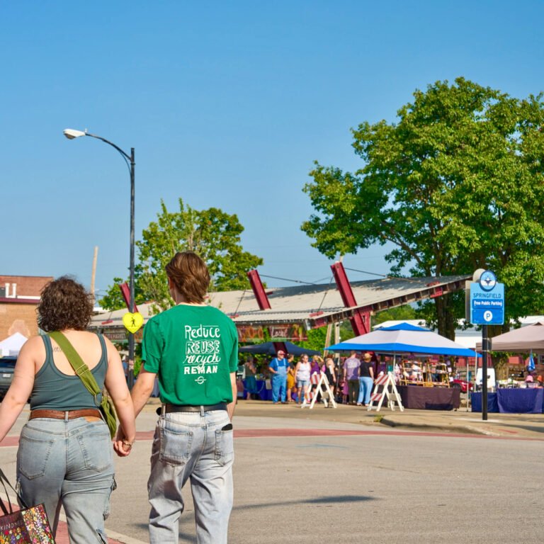 A couple walks hand in hand toward the C-Street City Market pavilion on a sunny summer morning.