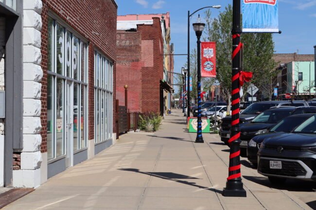 Red, white, and blue wrapped lampposts and banners line the C-Street sidewalk past brick storefronts.