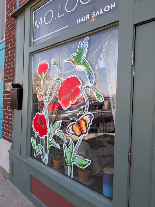 Painted poppies, a hummingbird, and a butterfly decorate the MO.LOCO Hair Salon window on C-Street.