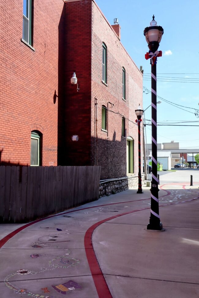 A red white and blue wrapped lamppost with a bow on a brick lined C-Street sidewalk in Springfield, Missouri.