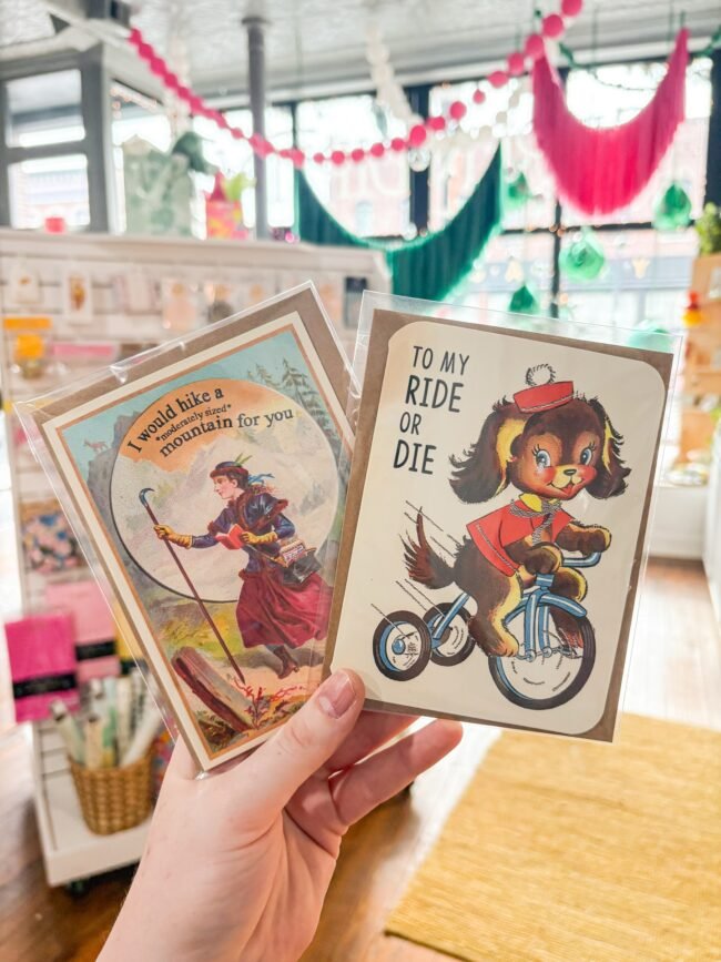 A hand holding illustrated greeting cards at the Serendipity shop on Historic C-Street, Springfield, MO.