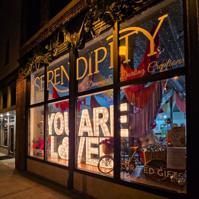 The Serendipity storefront on C-Street with a You Are Loved Valentine's window at night, Springfield, MO.