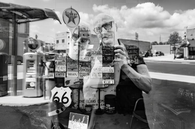 A black-and-white double-exposure Route 66 artwork with gas pumps and license plates, Two Voices One Road, MO.